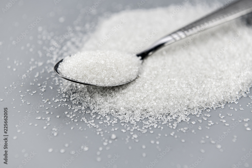 A spoonful of granulated sugar on gray background A spoonful of granulated sugar on gray background
