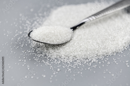 A spoonful of granulated sugar on gray background