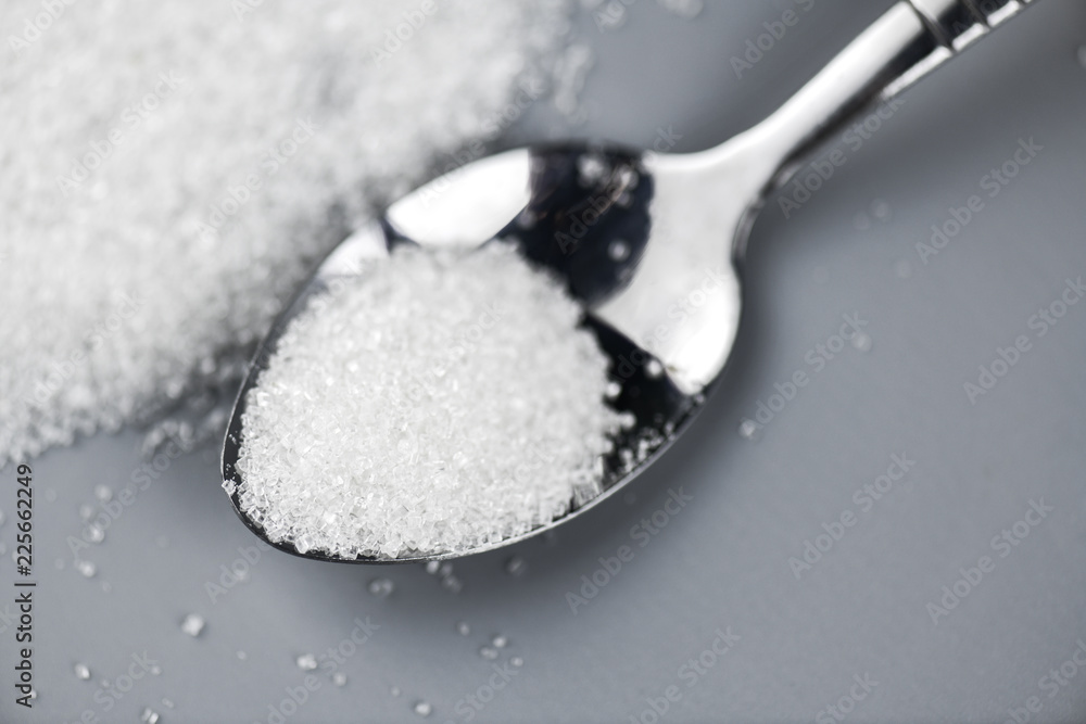 A spoonful of granulated sugar on gray background A spoonful of granulated sugar on gray background