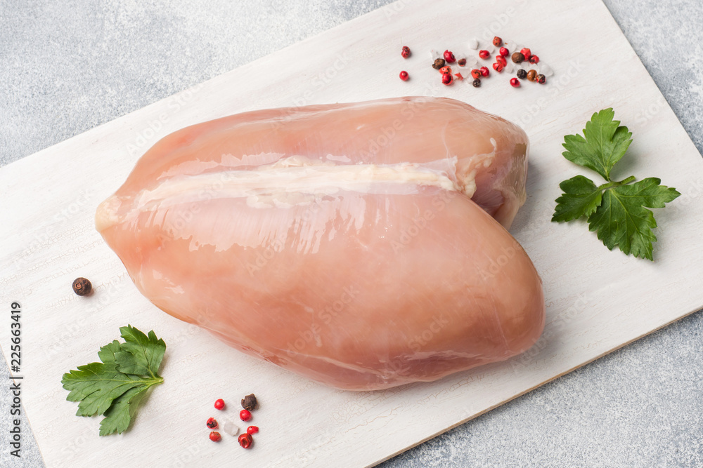 Raw chicken breasts and spices on wooden cutting board, close up view. Raw chicken breasts and spices on wooden cutting board, close up view.