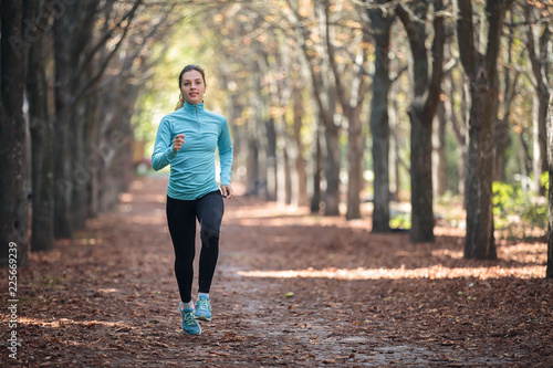 Athletic young woman runs in sportswear in the park in the fall.