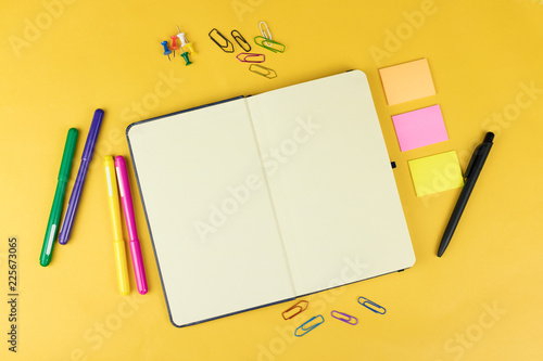 Top view of blank notebook and school supplies like colored markers, sticker and clipers on yellow background. . photo