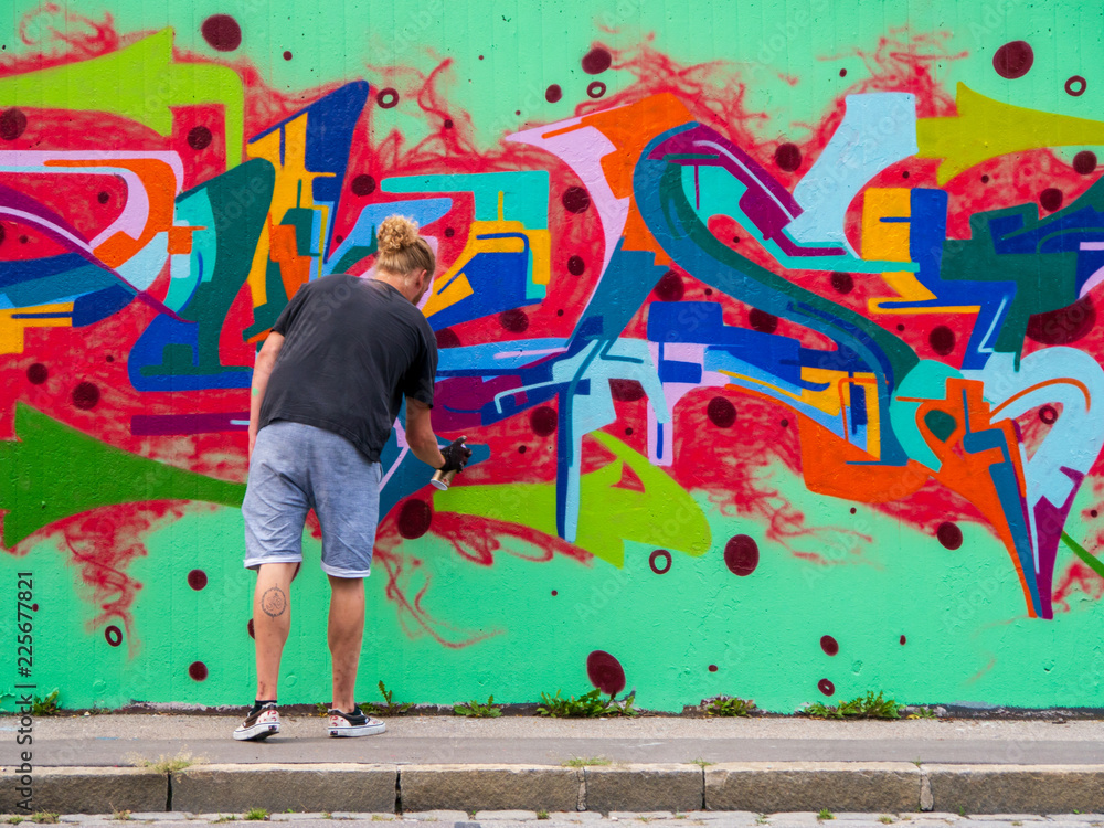 Fototapeta premium młody człowiek wykorzystuje swój talent i wyczucie sztuki, aby zastosować to w różnych kolorach na murze miejskim