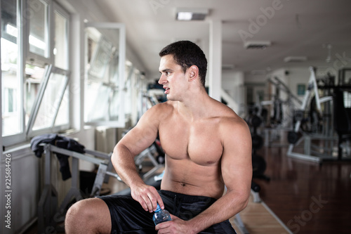Young attractive adult man exercising and doing weight lifting at fitness gym. Sport training indoors.