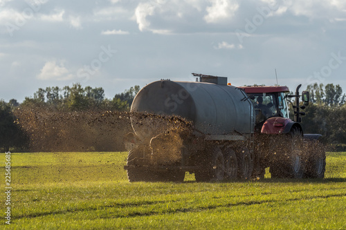 A farm tractor sprays its manure from the tanker onto a field. Manure is used as fertilizer in agriculture. Concept: agriculture