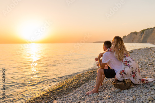 Young couple in love, man and woman enjoying romantic evening on the beach watching the sunset