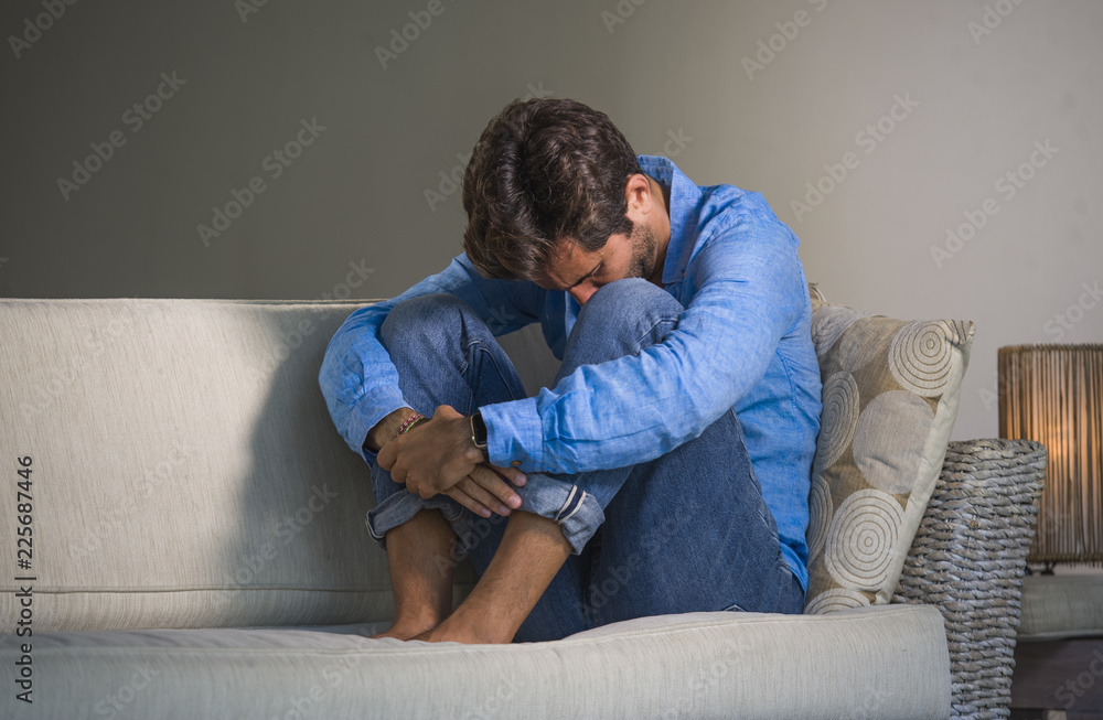 young attractive and handsome sad latin man sitting tired and depressed at home sofa couch feeling overwhelmed and worried suffering depression crisis and anxiety