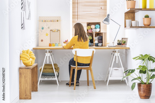 Woman sitting at a desk in a home office interior with knitting wool, organizer and yellow pillow © Photographee.eu