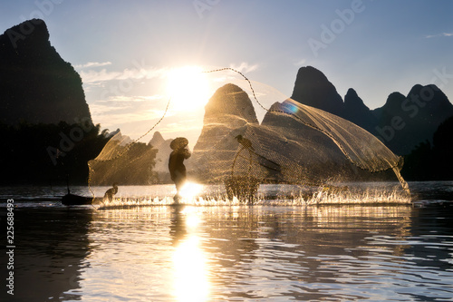 Leinwand Poster Cormorant fisherman on his bamboo raft at sunset