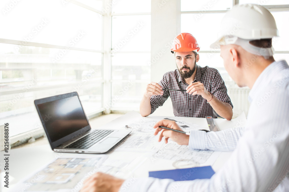 male engineers, architects working at the desk in helmets. Drawings, laptop, roulette on the desktop. Reception and supervision of building construction