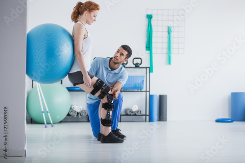 Woman with orthopedic problem exercising with ball while physiotherapist supporting her photo