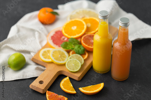 food , healthy eating and vegetarian concept - glass bottles of orange and grapefruit juice and citrus fruits on slate table top