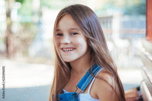 Little girl cheerful, laughs and sits on a bench in the park summer