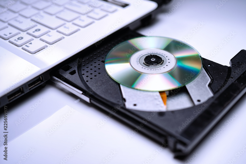 DVD Disk on the white Laptop DVD ROM Tray with a Man Hand. A Piracy conceptual image of burning data into DVD Disk DVD Disk on the white Laptop DVD ROM Tray with a Man Hand. A Piracy conceptual image of burning data into DVD Disk