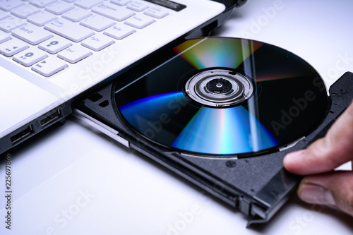 DVD Disk on the white Laptop DVD ROM Tray with a Man Hand. A Piracy conceptual image of burning data into DVD Disk