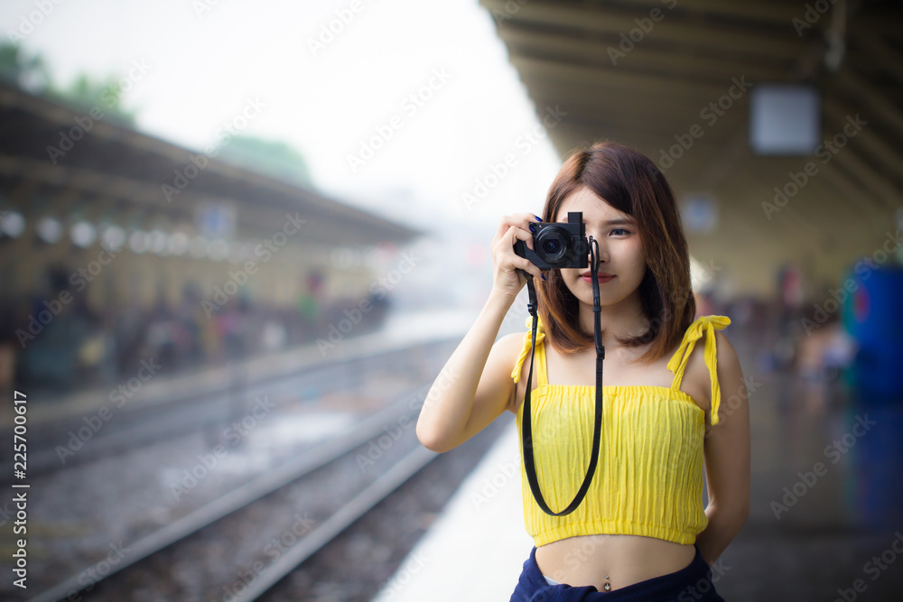 Young woman taking photo holding camera in hand. Young passenger at railway train station.