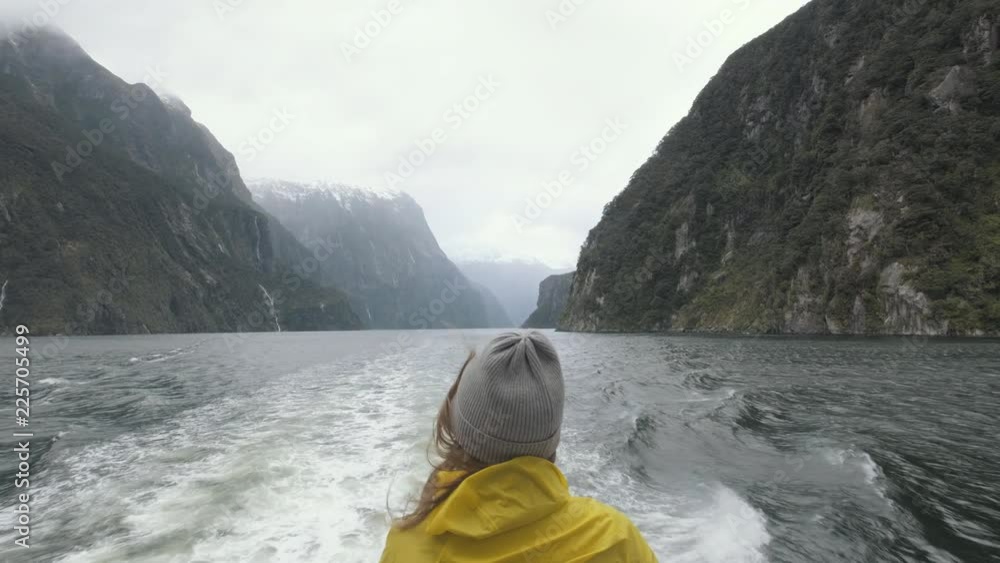 Girl in a bright yellow rain jacket standing on the back of a boat as ...