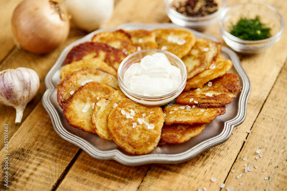 metal plate with delicious potato pancakes on an old wooden table with garlic onions and toppings in the kitchen metal plate with delicious potato pancakes on an old wooden table with garlic onions and toppings in the kitchen