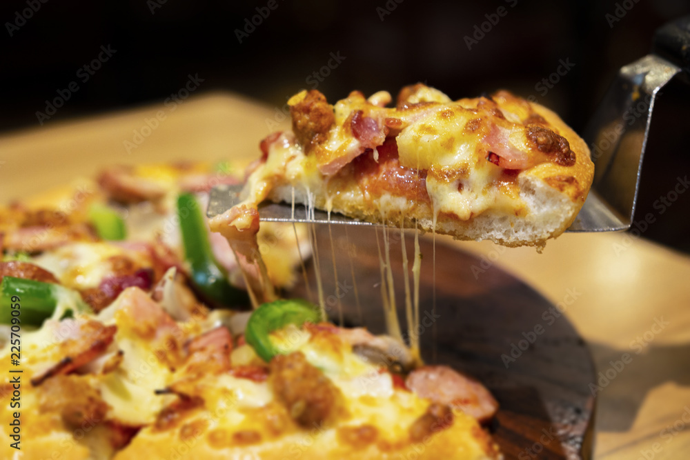 blurred image of Slice of hot pizza large cheese lunch or dinner crust seafood meat topping sauce. with bell pepper vegetables delicious tasty fast food italian traditional on wooden board blurred image of Slice of hot pizza large cheese lunch or dinner crust seafood meat topping sauce. with bell pepper vegetables delicious tasty fast food italian traditional on wooden board