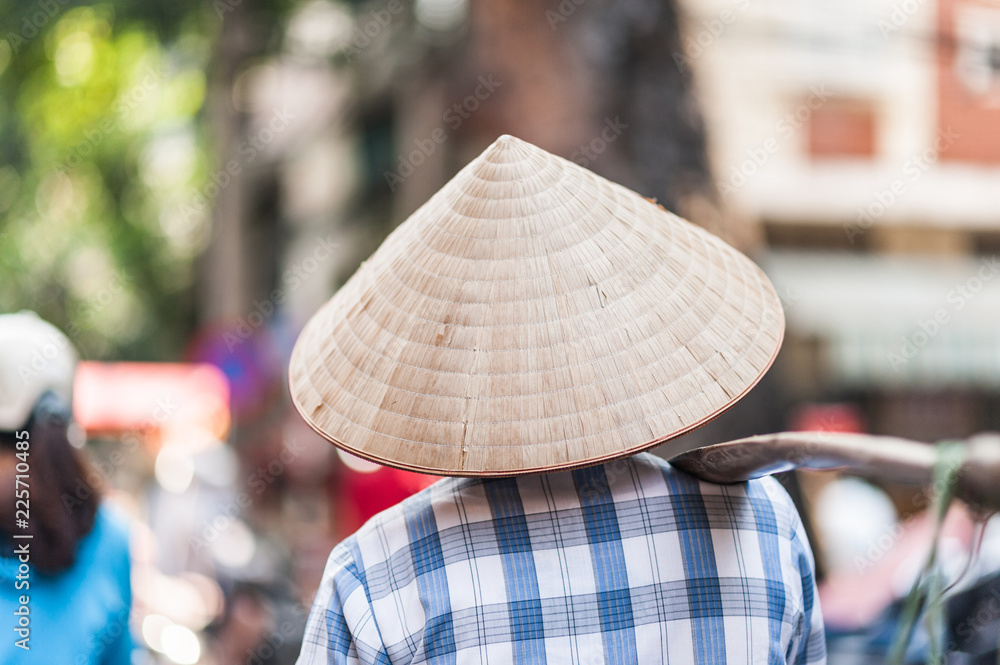Woman wearing a traditional woven rice hat on the streets of Hanoi, Vietnam.