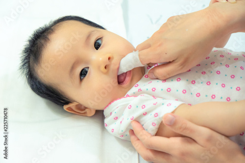 Mother use finger to clean asian baby tongue with clean gauze.