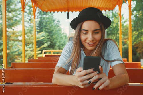 Young hipster girl in trendy hat holding smartphone in hands smi