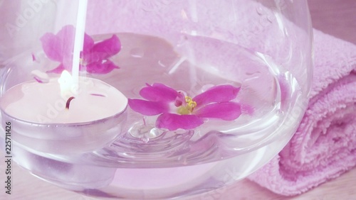 Romantic composition with a candle and violet flowers floating in a bowl of water.The concept of Spa cosmetic procedure treatment.