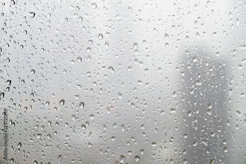 Rain drops on window glasses surface with cloudy background.