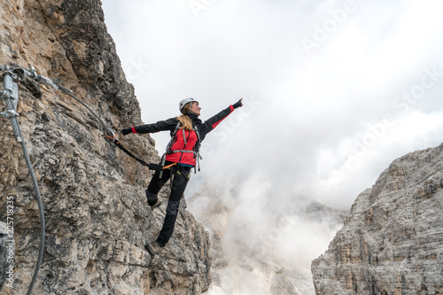 young attractive female university student on a vertical and exposed rock face climbs a Via Ferrata in Alta Badia in the South Tyrol