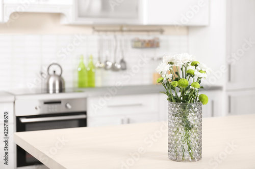 Vase with beautiful flowers on table in kitchen interior. Space for text