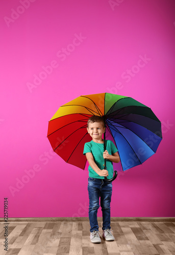 Little boy with rainbow umbrella near color wall