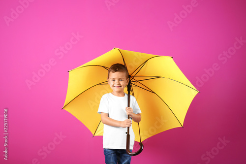 Little boy with yellow umbrella on color background