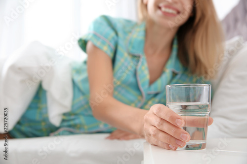 Woman with glass of clean water lying in bed at home, closeup