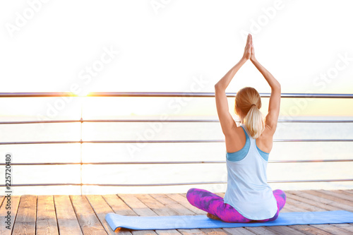 Fototapeta Naklejka Na Ścianę i Meble -  Young woman doing yoga exercises on pier in morning