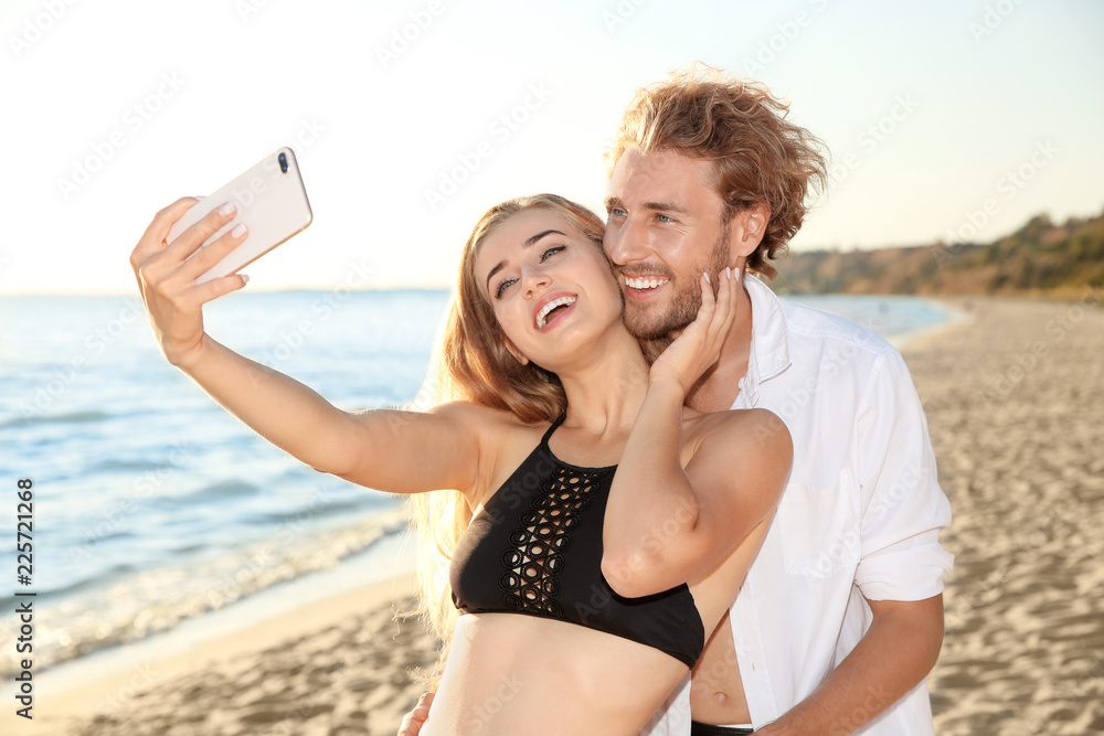 Happy young couple in beachwear taking selfie on seashore