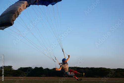 Skydiver under a dark blue and grey little canopy of a parachute is speed landing on airfield, close-up