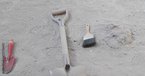 archeoogical elements over sandy soil beside fossil of head of dinosaur. Shovels and brushes placed over the soil ready to be used. Camera panning. Ischigualasto photo