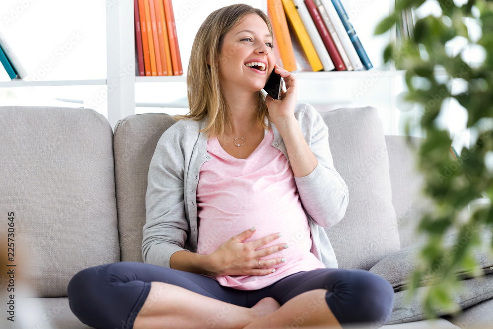 Beautiful young pregnant woman talking with her smartphone on the sofa at home