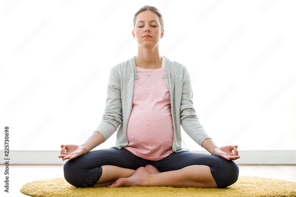 Beautiful pregnant woman relax doing yoga, sitting in lotus position at home Beautiful pregnant woman relax doing yoga, sitting in lotus position at home