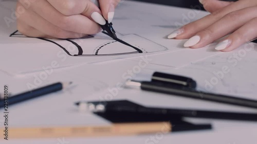 Attractive young woman sitting at the table in office, holding pencil and drawing sketch of shoes on paper. Shoes designer. 4K photo