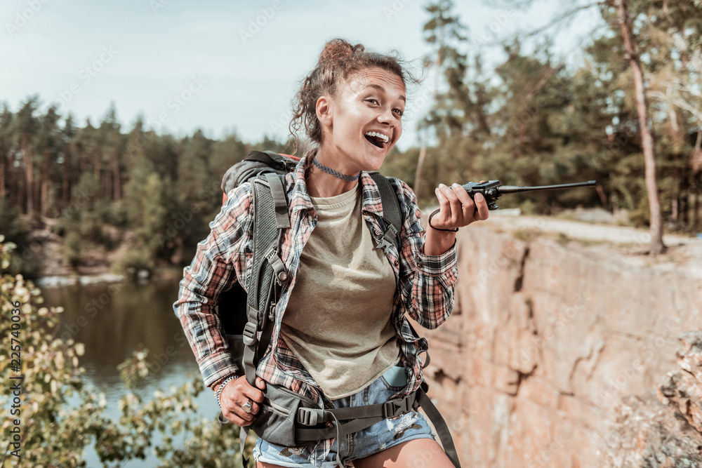 Naklejka premium Female hiker. Dark-haired female hiker wearing denim shorts and squared shirt using her pager while talking to her friend