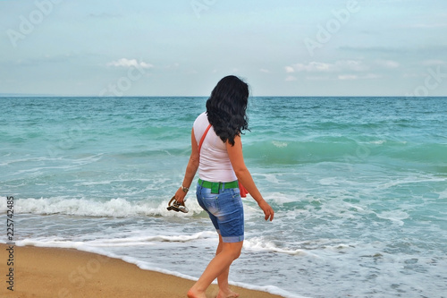 a young girl in a white Tshirt is walking along the sand in the sea. brunette on the shore of the azure sea in Bulgaria, golden sands