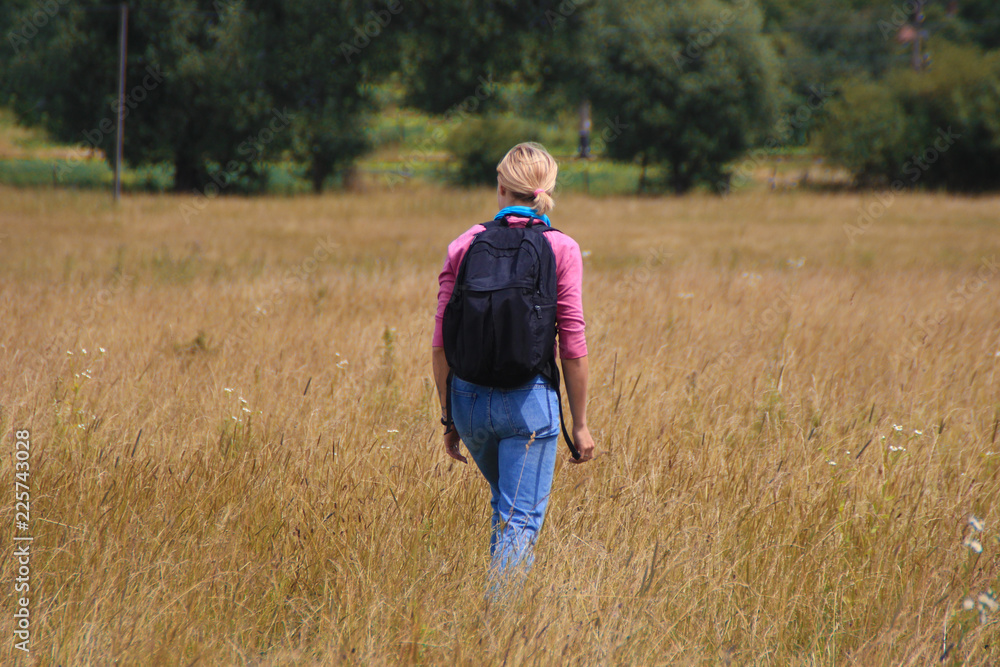 A girl with a backpack walks in the field with dogs. summer in the country field
