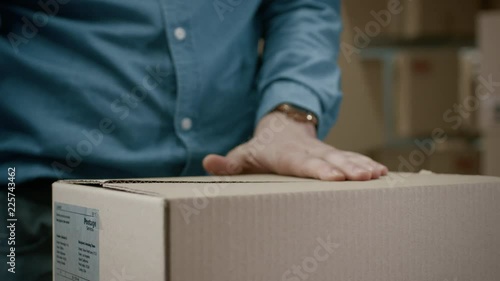 Close-up Shot of Professional Warehouse Worker Checks and Seales Cardboard Box Ready for Shipment. In the Background  Rows of Shelves with Cardboard Boxes with Ready Orders. photo