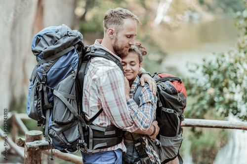Break in hiking. Loving handsome bearded backpacker hugging his appealing young woman while making break in hiking