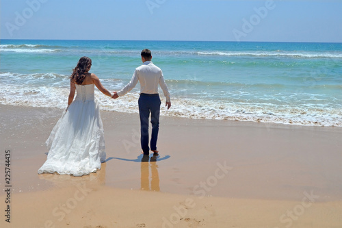 Long-haired brunette bride and groom in a suit. newlyweds holding hands  go to the sand in the water of the Indian Ocean. Wedding and honeymoon in the tropics on the island of Sri Lanka