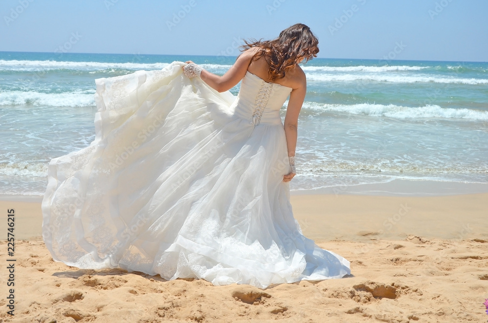 Long-haired brunette bride straightens her dress standing on the sand, the beach on the Indian Ocean. Wedding and honeymoon in the tropics on the island of Sri Lanka Long-haired brunette bride straightens her dress standing on the sand, the beach on the Indian Ocean. Wedding and honeymoon in the tropics on the island of Sri Lanka