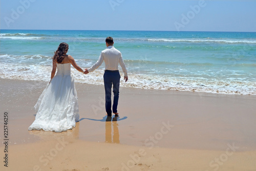 Long-haired brunette bride and groom in a suit. newlyweds holding hands, go to the sand in the water of the Indian Ocean. Wedding and honeymoon in the tropics on the island of Sri Lanka © SValeriia