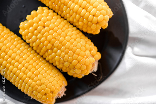 freshly boiled yellow corn on a black plate on a white background top view