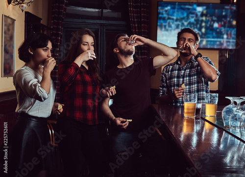 Young multiracial friends drink vodka, resting in the pub.